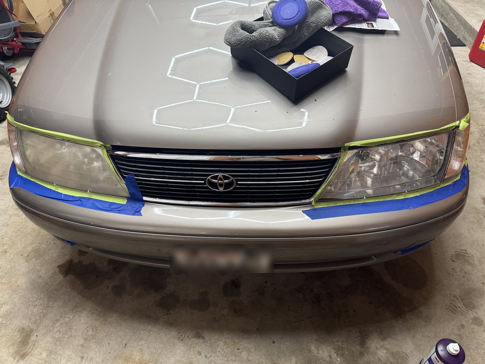 Headlight restoration in progress on a Toyota sedan — headlights taped off with sanding discs and polishing pads ready